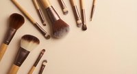 Professional makeup brushes set with wooden handles arranged on neutral beige background for beauty and cosmetics applications.