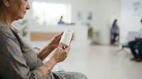 Senior woman with brown skin holding blank white smartphone in modern living room interior with blurred background, suitable for app promotion and technology advertising.