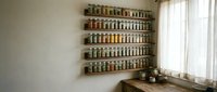 Organized spice rack with glass jars mounted on kitchen wall near window creating functional storage solution for cooking ingredients and herbs.