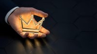 Businessman hand holding glowing golden crown symbol against dark background, representing success, leadership, achievement, and premium quality for business concepts.