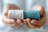 Female hands holding two rolls of natural linen fabric in white and turquoise colors against blurred background, showing sustainable textile materials.