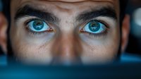 Close-up of young Caucasian man with striking blue eyes and intense gaze. Dramatic lighting highlights facial features for portrait photography.