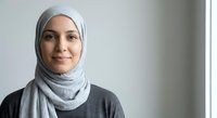 Young Muslim woman wearing gray hijab smiling confidently in modern office setting, professional portrait for business and diversity concepts.