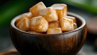 Golden caramel fudge pieces in wooden bowl with soft focus background, sweet homemade candy dessert closeup macro photography for food blogs.