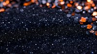 Glittering black background with scattered orange crystals and sparkles creating magical contrast. Dark moody surface with bokeh light effects and shimmering texture.