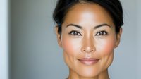 Professional Asian businesswoman with confident smile and natural makeup in modern office setting for corporate communications and marketing materials.