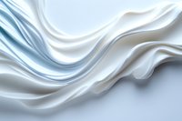 Elegant white silk fabric with soft flowing waves and gentle folds creates luxurious abstract background texture in light blue and pearl tones.