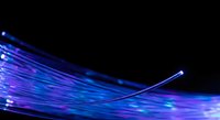 Abstract blue and purple fiber optic cables with glowing light streaks creating dynamic motion blur effect on black background for technology concepts.