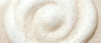 Creamy white foam swirl texture with delicate bubbles on a beige surface, capturing a soft spiral pattern for beauty, spa, or cosmetic backgrounds.