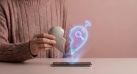 Woman in beige sweater using smartphone with holographic GPS location pin icon floating above device for navigation and mapping technology concepts.