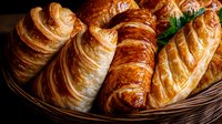 Fresh baked croissants and puff pastry in wicker basket, golden brown flaky layers with buttery shine, close up view on dark background for bakery menu.