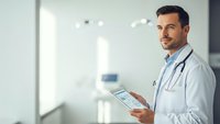 Confident male doctor with tablet in modern hospital corridor. Healthcare professional using digital technology for patient care and medical records.