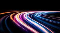 Colorful light trails curve against dark background creating dynamic motion effect. Long exposure photography shows streaks of blue, purple, orange and pink neon lights.