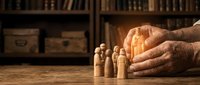 Elderly hands protecting wooden family figures on rustic table with vintage library background symbolizing care, guardianship and family protection.