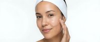 Young Asian woman applying facial cream with white headband on clean background for skincare beauty routine and cosmetic product advertising.