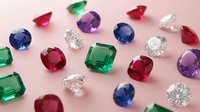 Colorful collection of precious gemstones including emeralds, rubies, sapphires, amethysts and diamonds scattered on pink background for jewelry design.