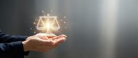 Businessperson holding glowing scales of justice symbol with golden light particles, representing law, fairness, legal services, and ethical business practices.
