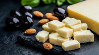 Cubed cheese pieces with almonds and dark grapes on black slate board, macro food photography for restaurant menu, gourmet appetizer presentation.