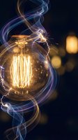 Vintage Edison bulb with glowing filament surrounded by colorful electric energy streams and sparks on dark background with bokeh lights.