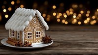Homemade gingerbread house with white icing roof on wooden table against blurred golden bokeh lights, decorated with cinnamon sticks and star anise.