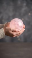 Person holding polished rose quartz sphere in cupped hands against blurred background with bokeh lights. Suitable for wellness, spirituality, healing, and mindfulness content.