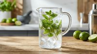 Fresh mojito cocktail with mint leaves and ice cubes in glass pitcher on wooden counter, refreshing summer drink for bar and restaurant service.