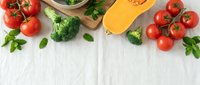 Fresh vegetables frame with tomatoes, broccoli, butternut squash and herbs on white marble background for healthy cooking and meal preparation.