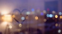 Heart shape drawn on foggy window glass with romantic bokeh lights and warm sunset glow creating dreamy atmosphere for love and romance concepts.