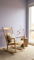 Wooden rocking chair with cream cushions in lavender bedroom with natural light from glass door, minimalist nursery or relaxation space.