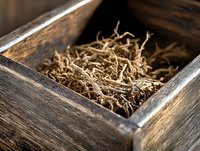 Dried medicinal roots in vintage wooden box, close-up view showing natural herbal medicine ingredients with textured organic material and rustic storage container.