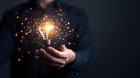 Businessman holding glowing light bulb with sparkling orange particles, symbolizing innovation and creative business solutions on dark background.
