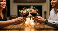 Happy couple toasting with red wine glasses at romantic dinner date with candles creating intimate atmosphere for celebration and connection.