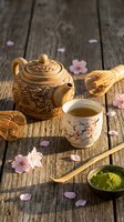 Traditional Asian tea ceremony setup with ornate clay teapot, delicate cup, bamboo whisk and matcha powder on rustic wooden table decorated with pink cherry blossoms.