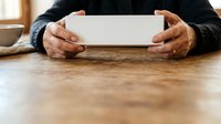 Middle-aged man with dark skin tone wearing black sweater holding blank white tablet device on wooden table surface indoors.
