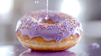 Glazed donut with purple frosting and colorful sprinkles on blurred background, liquid drop falling onto sweet pastry in macro photography.