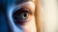 Close-up of woman's green eye with long eyelashes in dramatic lighting. Macro photography showcasing natural beauty and human expression for wellness concepts.