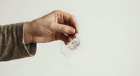 Hand holding transparent glass Christmas ornament ball against neutral background for holiday decorating and craft projects.