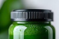 Fresh green smoothie or juice in glass bottle with black lid, condensation droplets on surface, macro shot with selective focus and blurred background.
