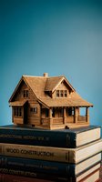 Miniature wooden house model sitting on stack of architecture books against blue gradient background for real estate and construction concepts.