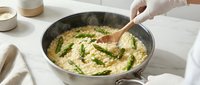 Cook stirring creamy hummus with fresh herbs and wooden spoon in pan, food preparation and cooking process.