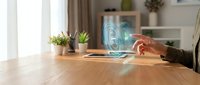 Young woman hand touching glowing holographic digital interface above tablet on wooden desk, futuristic technology concept in modern home office.