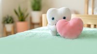 Cute white tooth character holding pink heart on mint green surface in cozy home interior with plants. Dental health care love concept for children education.