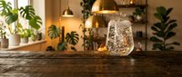 Sparkling water splashing in a clear glass on a rustic wooden table, warm cozy interior with green plants and golden pendant lights.