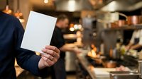 Businessman holding blank white card in modern kitchen restaurant setting with warm lighting and blurred background for branding mockup purposes.