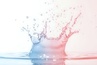 Dynamic water splash collision creating mirror effect in blue and red gradient colors against white background, with droplets frozen in motion showing liquid surface tension.