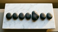 Smooth dark stones arranged in a row on white marble surface for wellness, spa, meditation, and relaxation therapy applications.