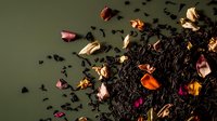Loose black tea leaves scattered with vibrant dried rose petals and flower buds on dark green background, creating aromatic composition for tea packaging design.