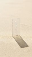 Transparent acrylic card with promo text standing upright in golden sand, casting a long shadow in warm sunlight for summer sale concepts.