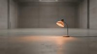 Single desk lamp with warm glow illuminating empty concrete floor in minimalist industrial space, suitable for office, workspace, and interior design projects.