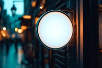 Blank circular storefront sign mounted on building facade at dusk with blurred street lights and urban background, suitable for branding and advertising mockups.